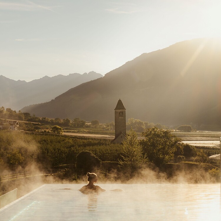 Frau genießt im Infinity Skypool die traumhafte Aussicht bei Sonnenaufgang