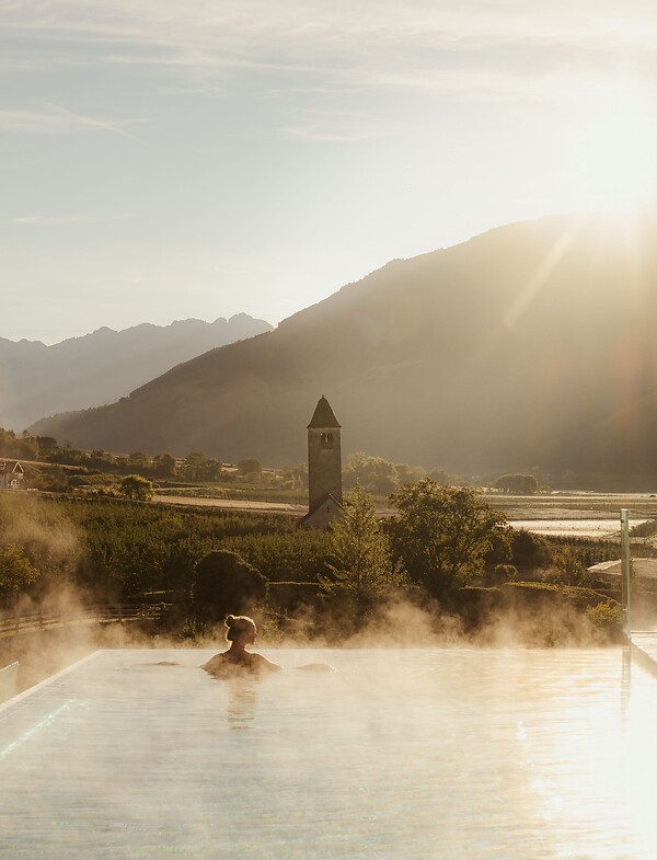 Frau genießt im Infinity Skypool die traumhafte Aussicht bei Sonnenaufgang