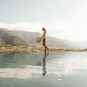 Frau spaziert am Infinity Pool entlang mit einem endlosen Panoramablick