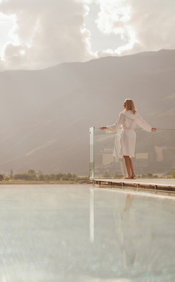 Frau steht an Sky Infinity Thermalpool vor Bergpanorama