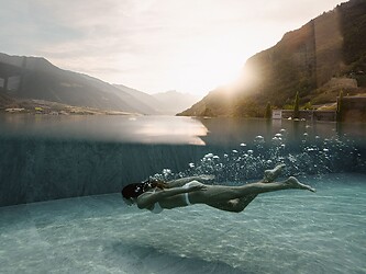 Frau schwimmt unter Wasser im Infinity Pool bei Sonnenuntergang