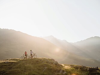 Frau und Mann mit Rad im Berg vor untergehender Abendsonne